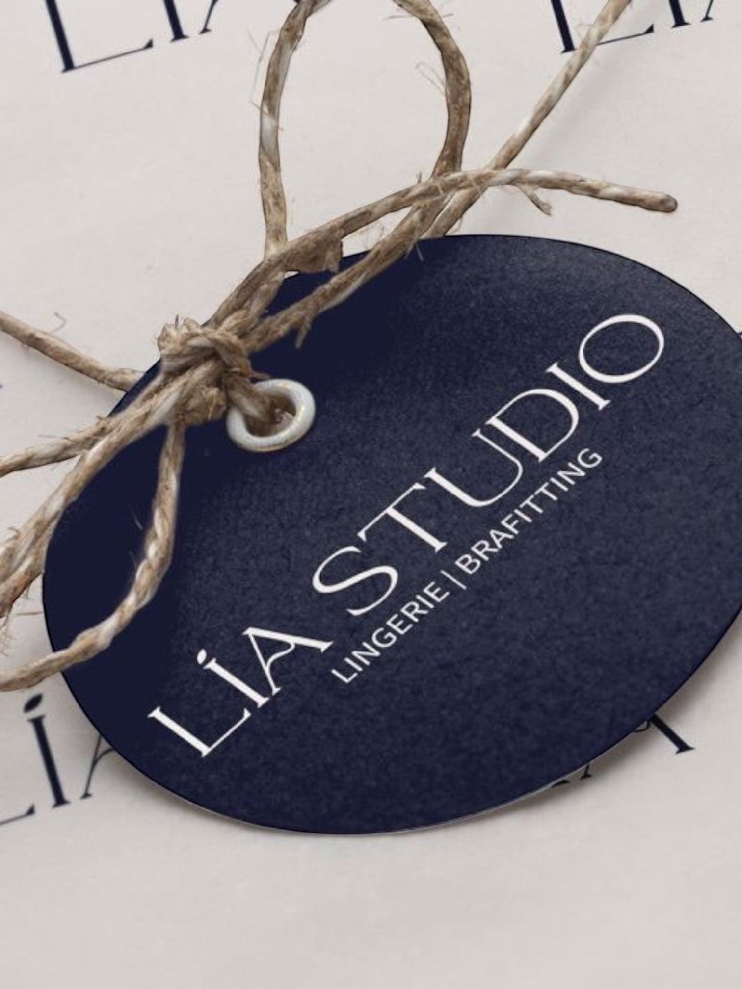LIA STUDIO LINGERIE branded dark blue oval gift tag with rustic twine string on white wrapping paper
